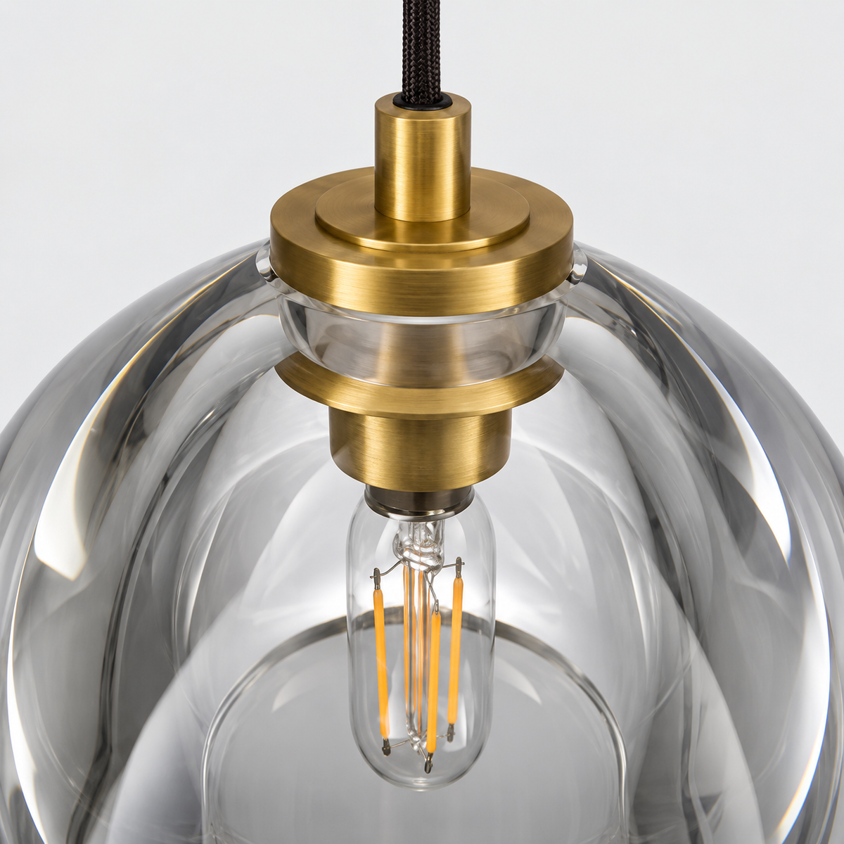 Close-up of a pendant light with a clear glass dome shade, brass metal fixture, and visible filament bulb against a light gray background.