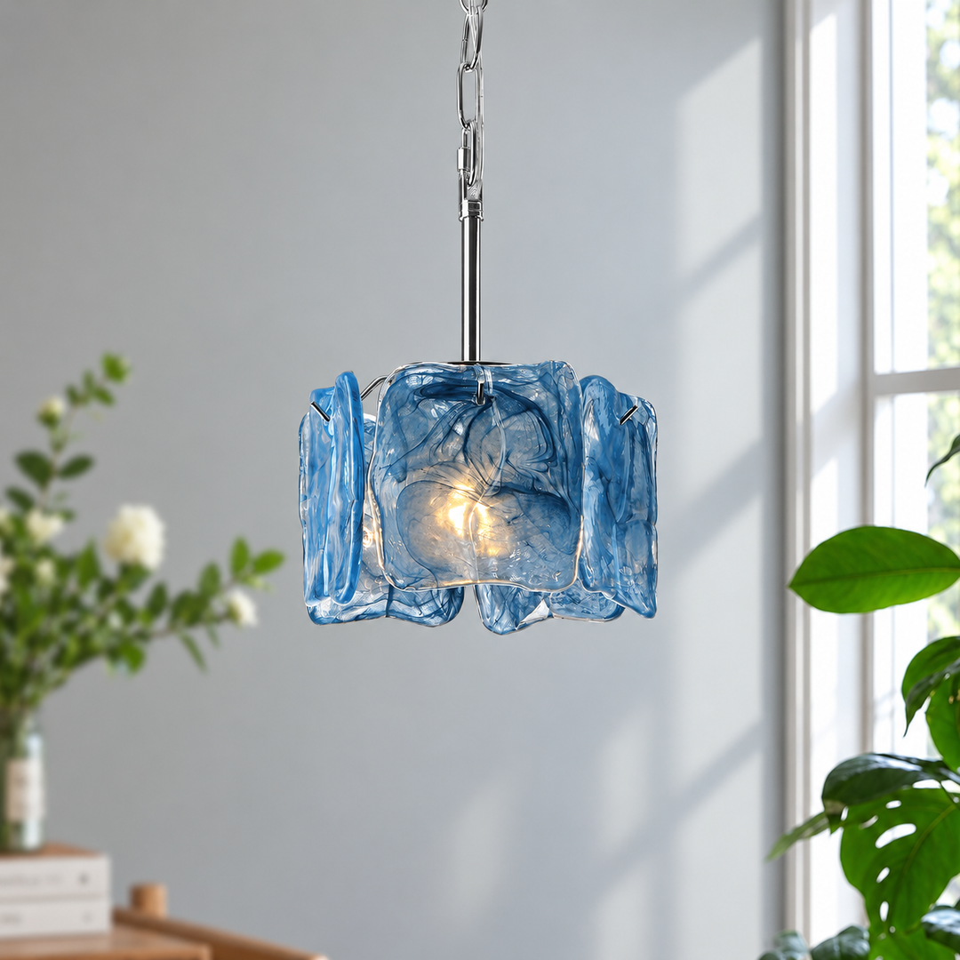A blue textured glass pendant light with a silver metal chain and rod, hanging in a bright room with a window and plants in the background.