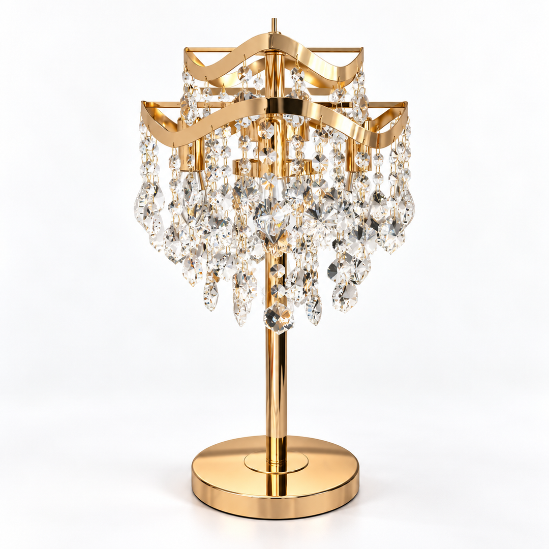 A gold-finished table lamp with a tiered crystal chandelier design, featuring clear faceted hanging prisms on a round base, photographed against a seamless white background.