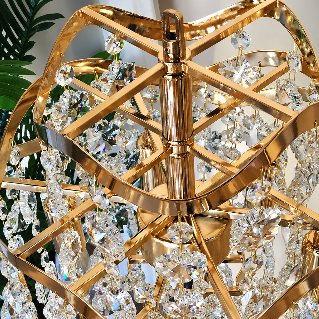 Close-up of a gold table lamp with curved framework and cascading clear crystal drops, with green foliage in the background.