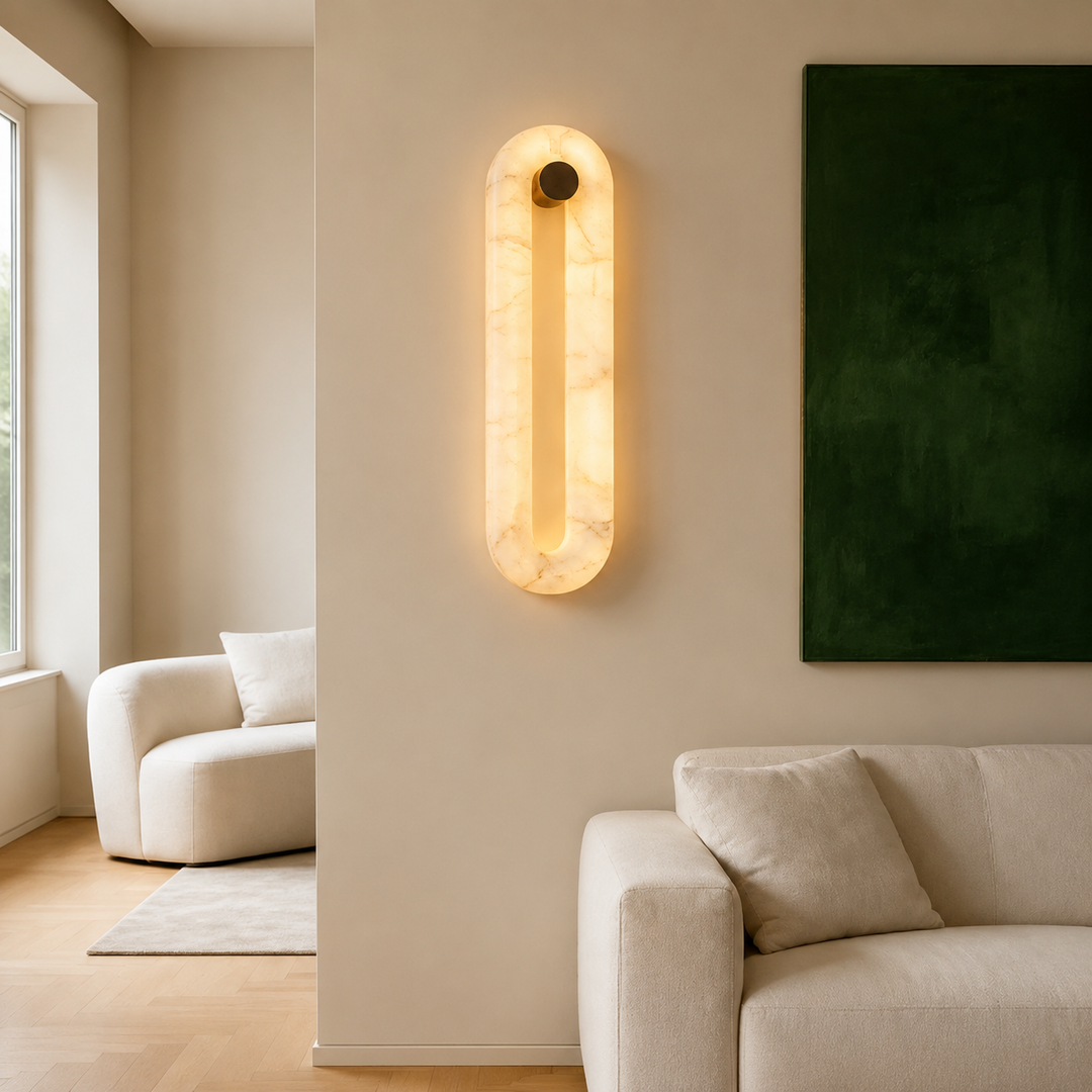A modern wall-mounted sconce with a warm glowing oval frame made of light marble, installed on a beige wall in a minimalist living room setting.