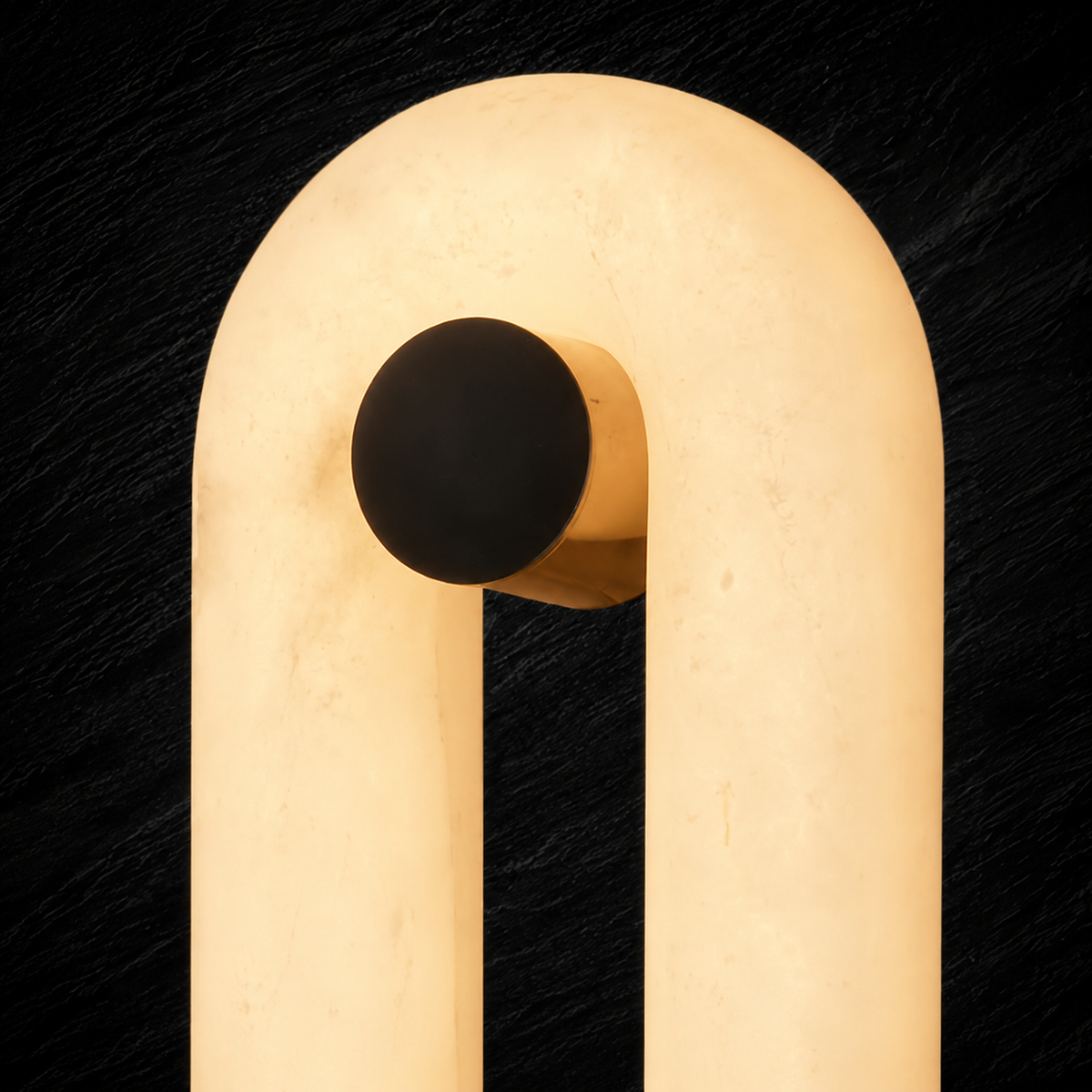 A modern wall sconce featuring a warm, glowing cream-colored U-shaped tube with a matte black spherical accent on the side, mounted against a dark textured background.