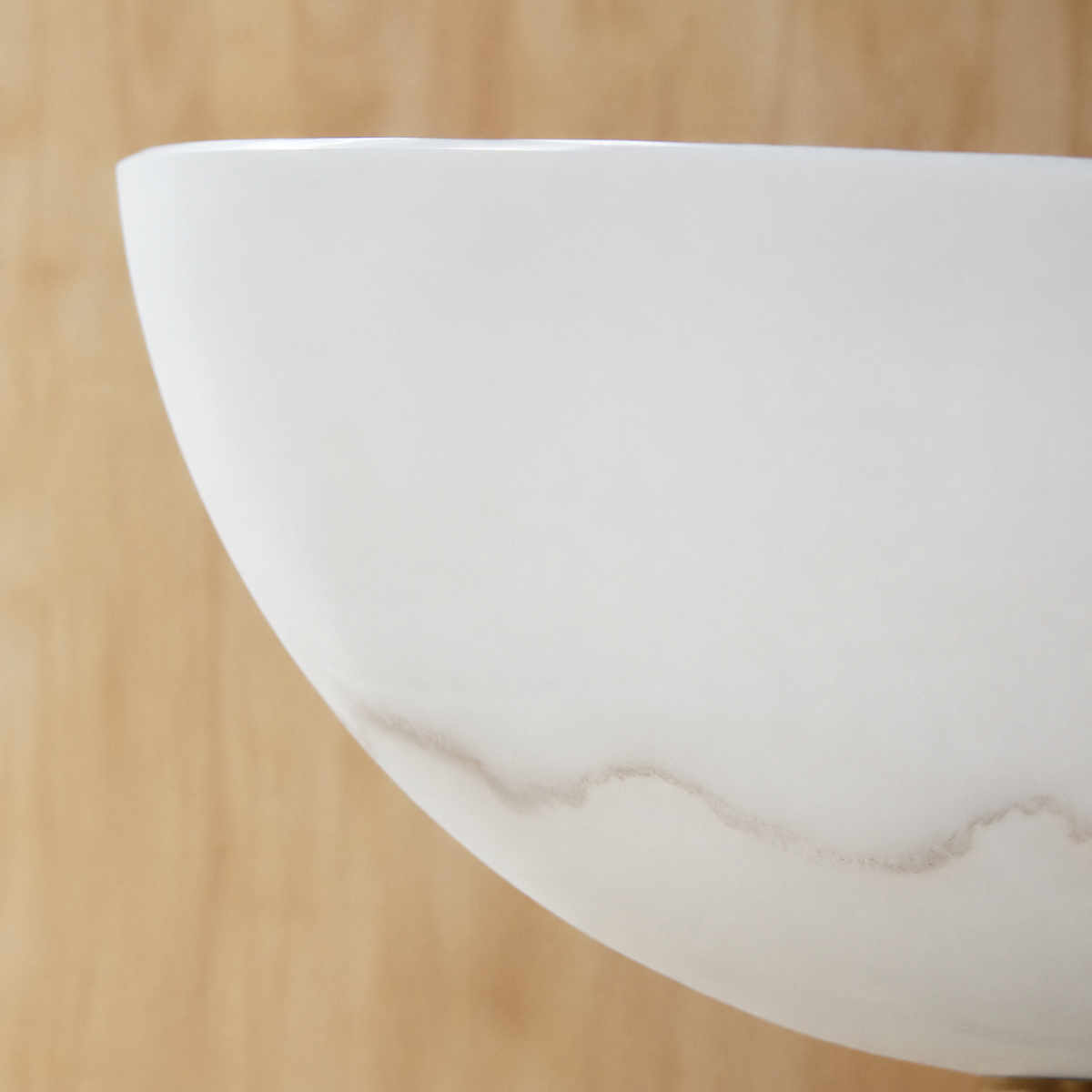 Close-up of a wall sconce's curved white Spanish alabaster shade with soft gray veining, set against a light wood background.