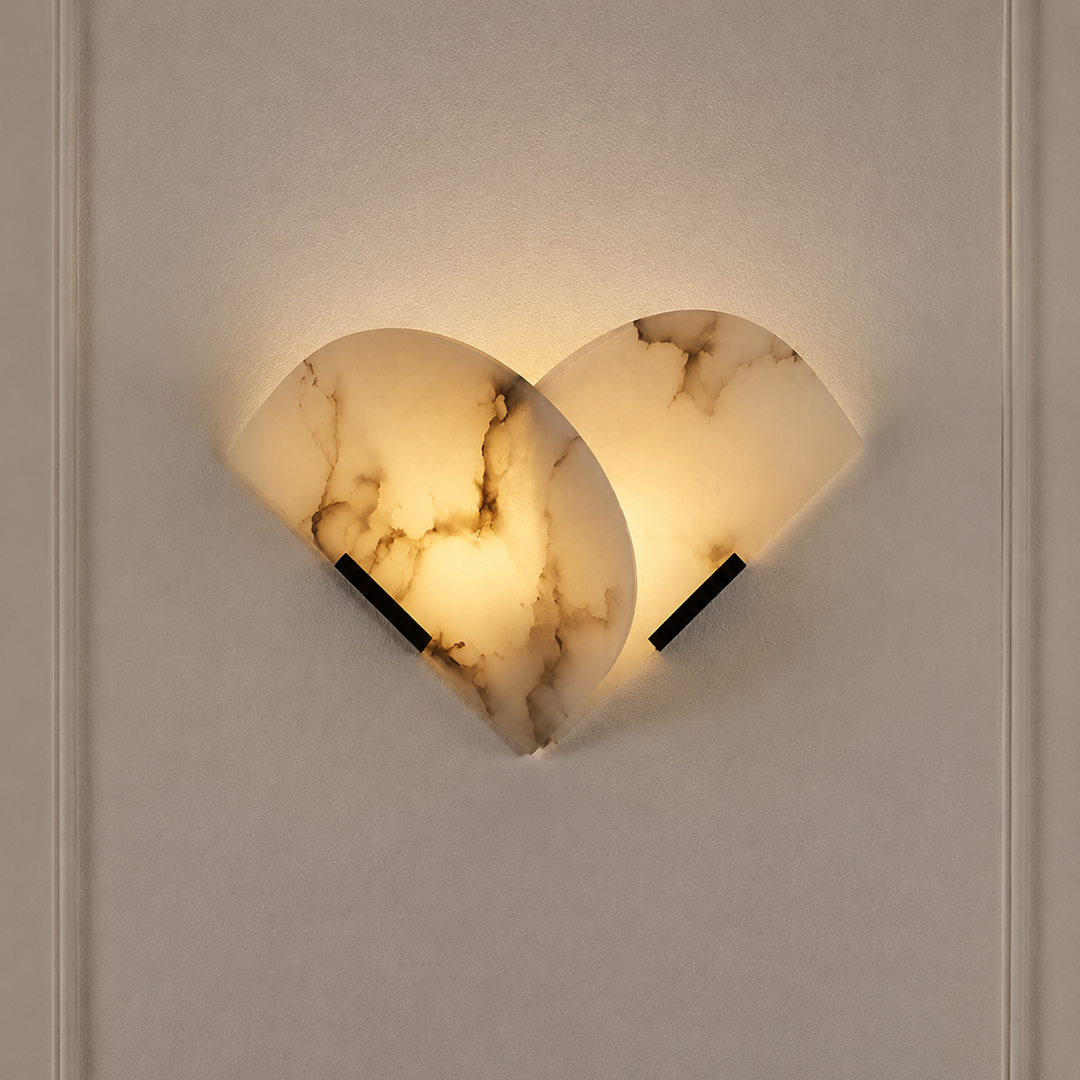 Wall sconce with overlapping cream alabaster panels, brown veining and black iron supports glows warmly against a pale paneled wall.