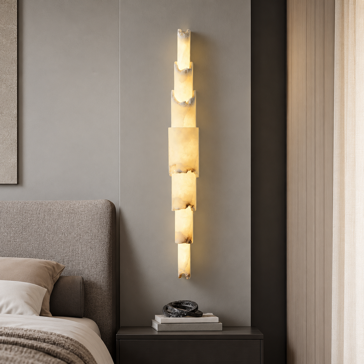 A modern vertical wall sconce with stacked rectangular illuminated stone or acrylic panels, mounted on a gray bedroom wall above a dark nightstand.