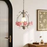 Silver-tone pendant light with pink glass flowers hanging in a room beside a black-framed door and framed botanical artwork.