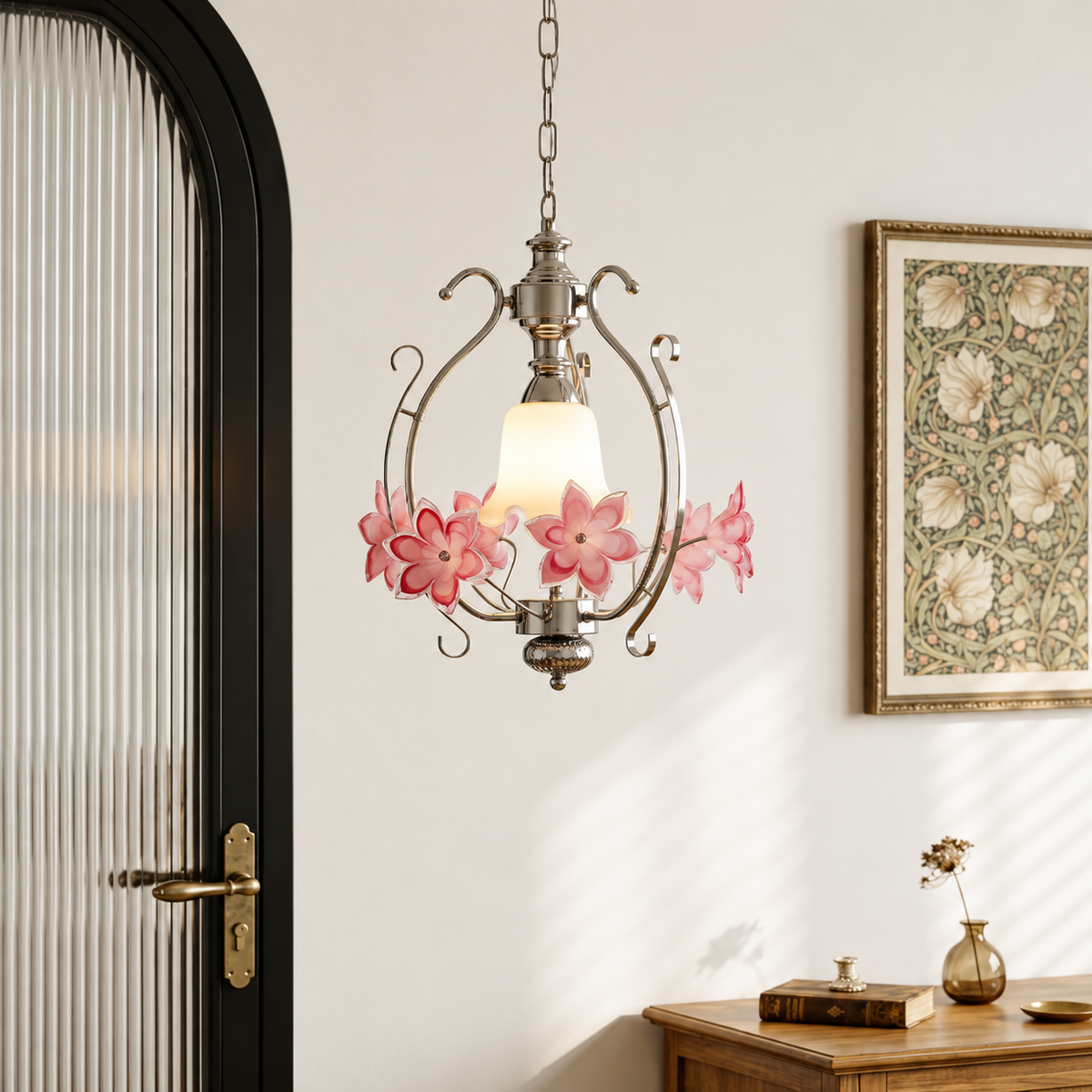 Silver-tone pendant light with pink glass flowers hanging in a room beside a black-framed door and framed botanical artwork.