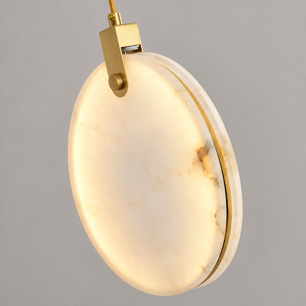 An oval pendant light with a warm white marble-look glass panel and polished gold metal hardware, shown against a neutral gray background.