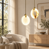 Two modern pendant lights hang in a bright, contemporary living room. One light has a warm, brushed gold finish, while the other has a frosted white glass globe shade.