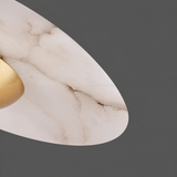 Close-up of a pendant light’s white veined alabaster disc shade and gold-toned center against a dark gray background.