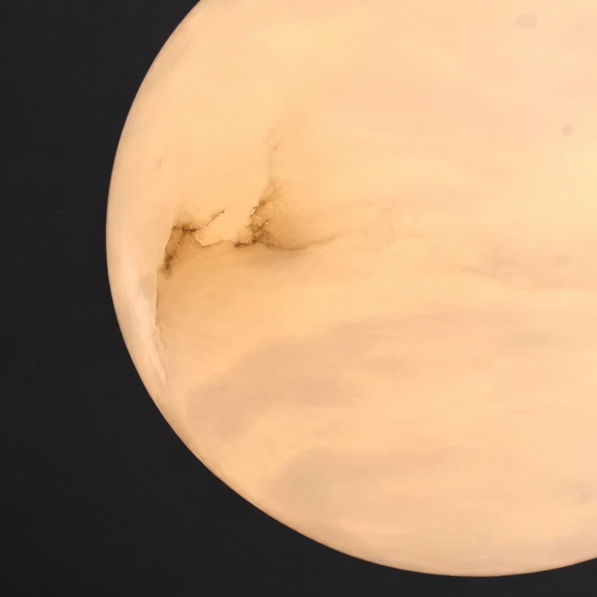Close-up of the pendant light’s rounded alabaster shade, glowing pale peach with visible veining against a black background.