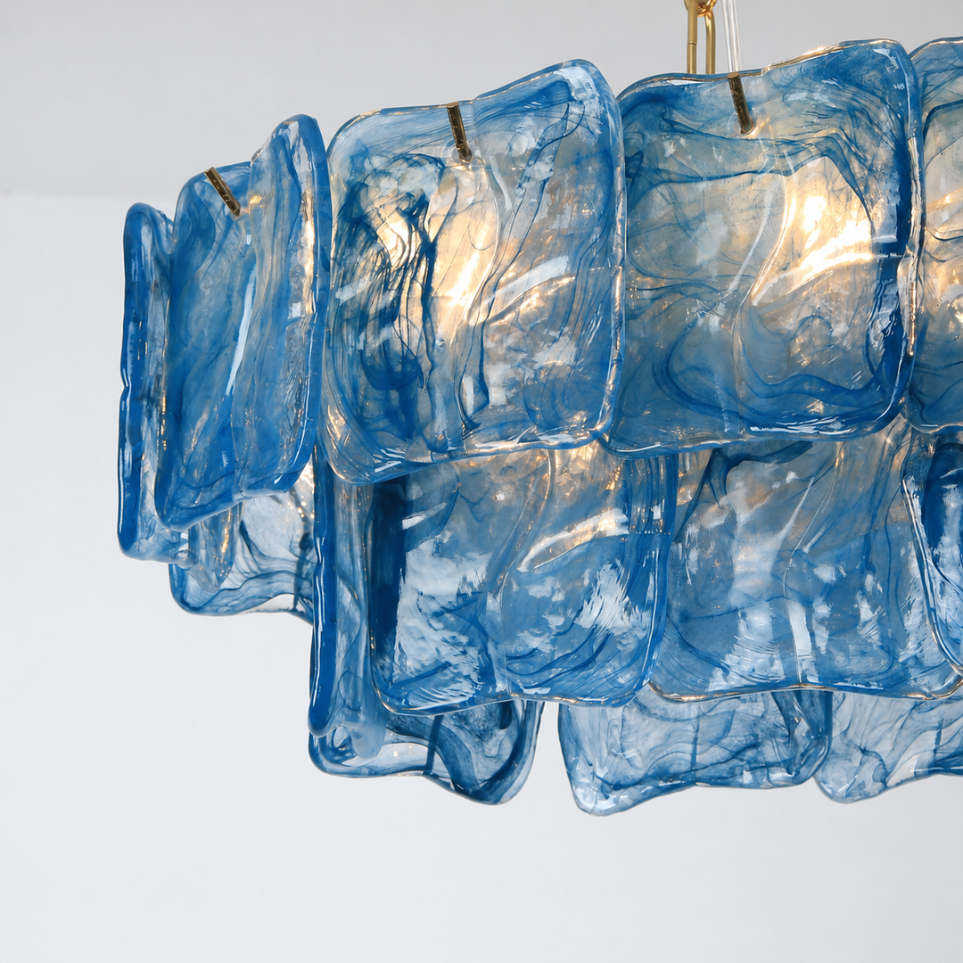 Close-up of the linear chandelier shows overlapping blue glass panels with swirling patterns and light shining through.