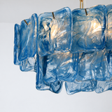 Close-up of the linear chandelier shows overlapping blue glass panels with swirling patterns and light shining through.