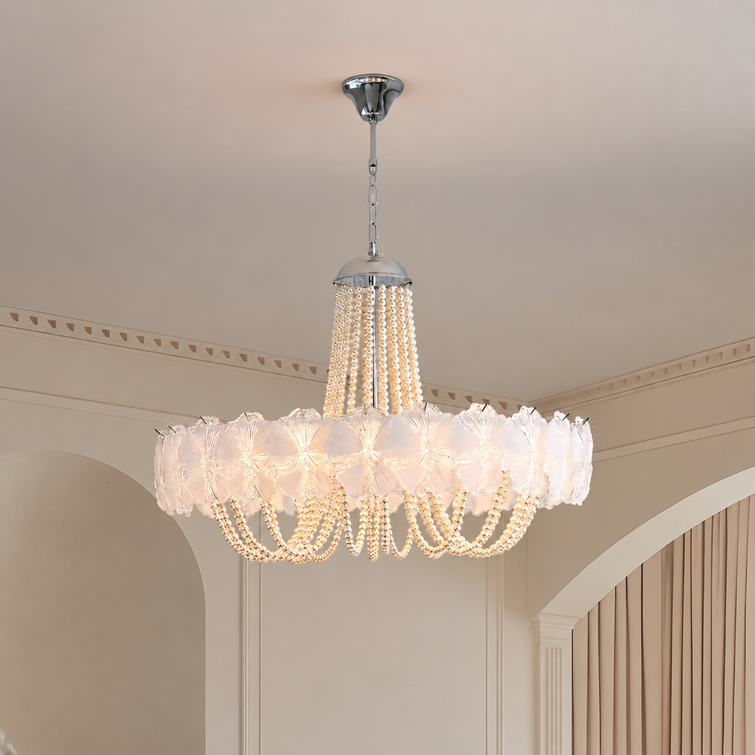 A large round chandelier with white ruffled glass shades and cascading pearl-like bead strands, hanging from a silver ceiling canopy in an elegant interior room.