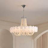 A large round chandelier with white ruffled glass shades and cascading pearl-like bead strands, hanging from a silver ceiling canopy in an elegant interior room.