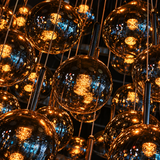A close-up of multiple hanging metallic glass chandelier globes glowing with warm amber light against a dark background.