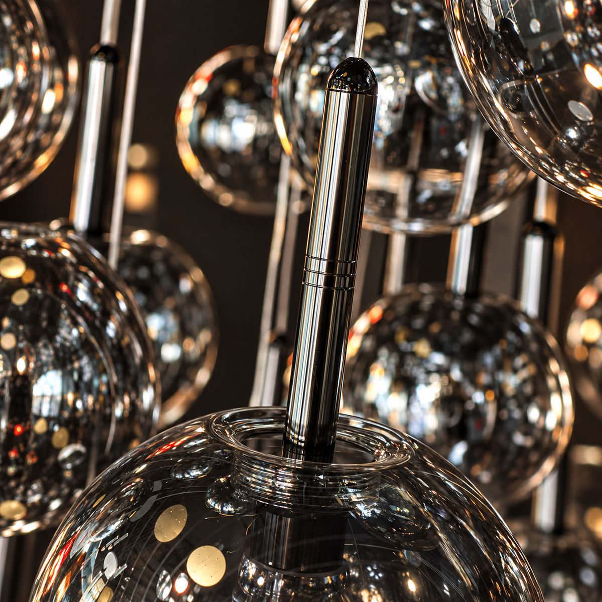 Close-up of a modern chandelier with large reflective glass globes and polished metallic stems, showing mirrored reflections and warm light points against a dark background.