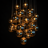 Chandelier with reflective amber-tinted globes and warm glowing lights suspended at varied heights against a black background.