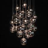 A modern chandelier featuring multiple clear glass spherical pendant lights of varying sizes, suspended from thin metal rods against a solid black background.