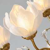 Close-up of a chandelier with illuminated white textured glass flower-shaped shades and gold metal arms, with clear crystal drops visible against a light gray background.