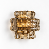 A modern wall sconce light fixture made of wavy, translucent smoky amber glass, shown against a plain white background.