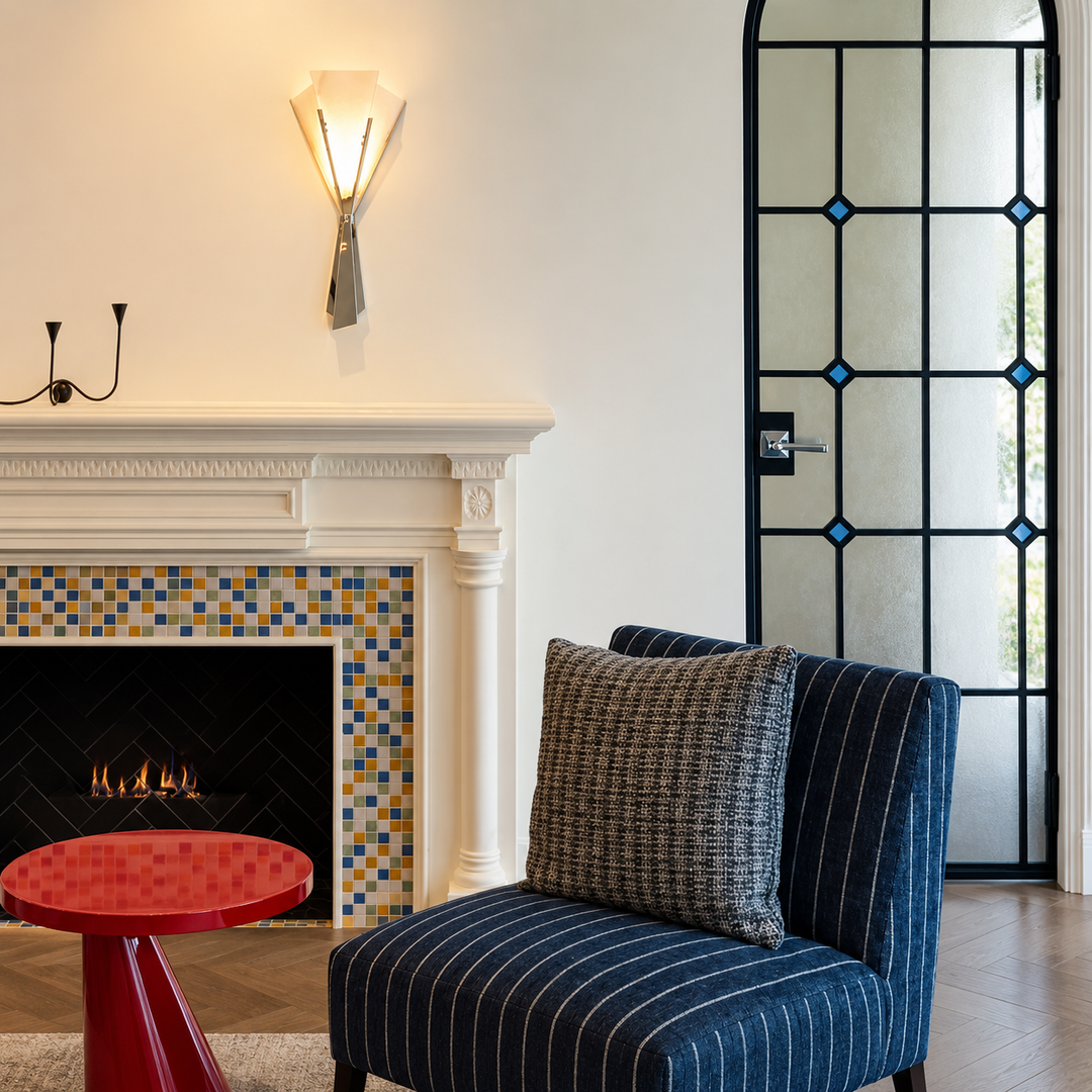 Illuminated alabaster wall sconce with polished stainless steel framing above a tiled fireplace beside a blue striped chair.