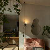 Red floor lamp glowing beside a pink lounge chair, irregular wall mirror, and leafy plants.