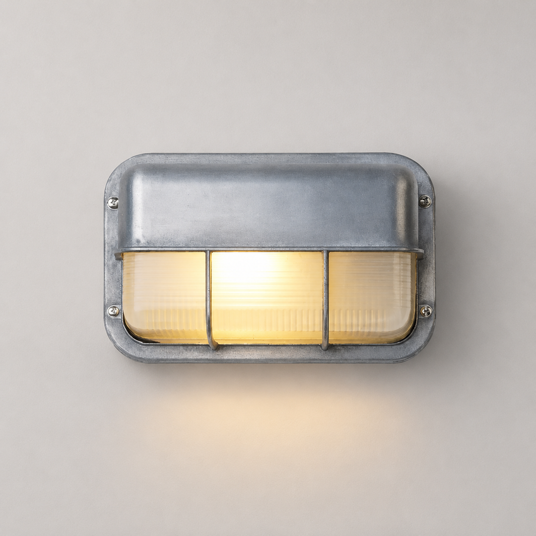 A rectangular industrial wall sconce with a galvanized steel frame and three illuminated frosted glass panels, mounted on a neutral light gray wall.
