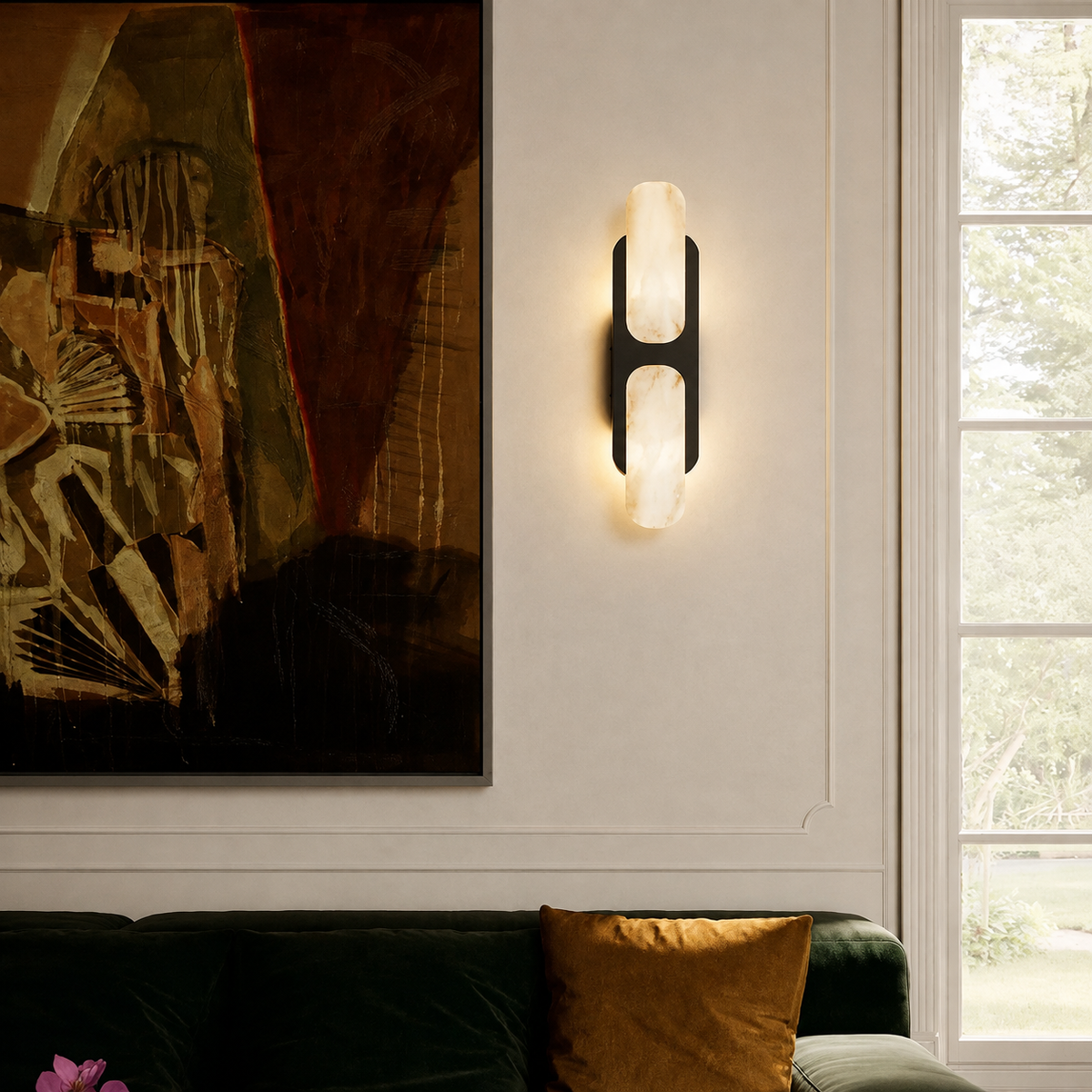 A modern wall-mounted sconce with two glowing oval light panels set in a black frame, mounted on a white wall in a styled living room next to a window and an abstract painting.