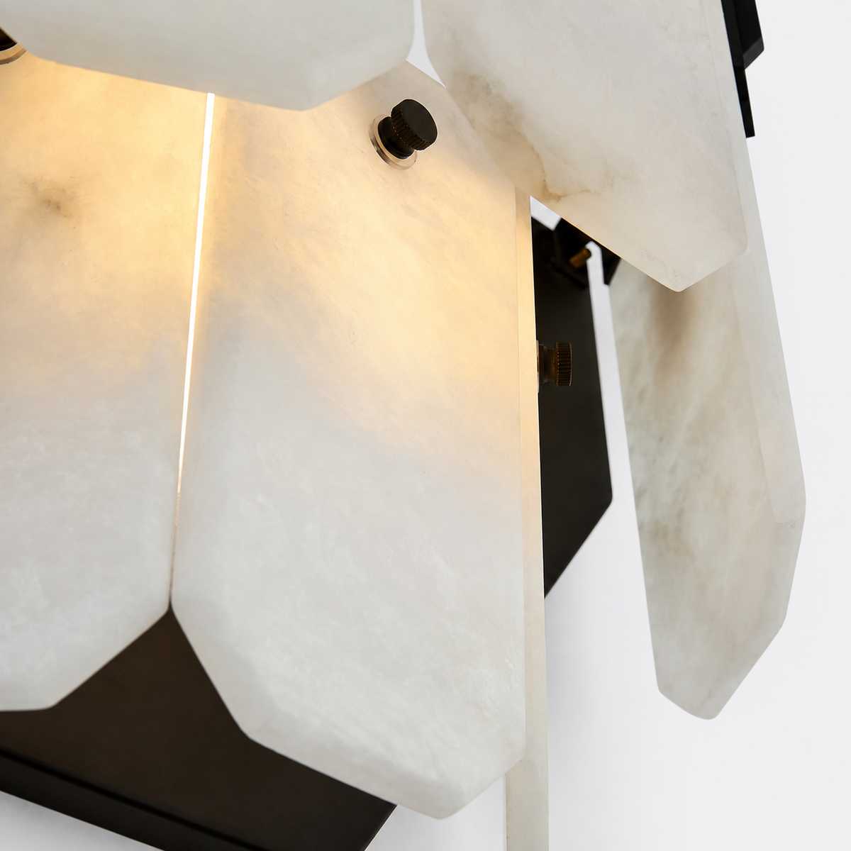Close-up of a modern wall sconce with translucent white stone or acrylic geometric panels and a dark metal frame, illuminated from within.