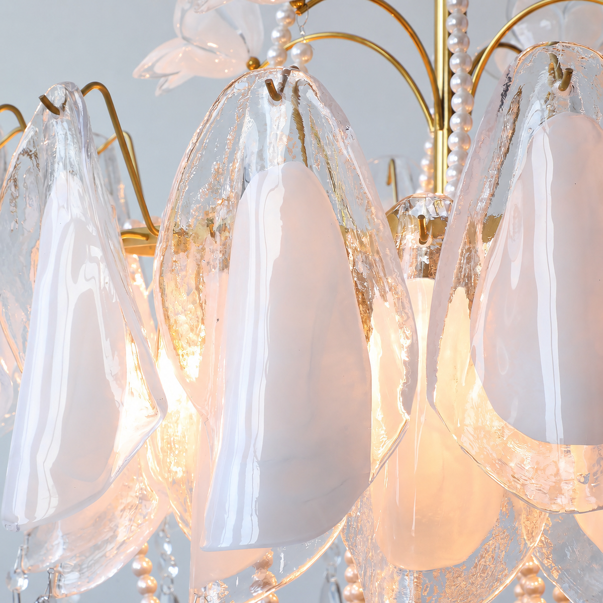 A close-up of a chandelier with teardrop-shaped translucent white glass shades, a gold metal frame, and warm glowing light inside.