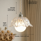 A clear glass flower-shaped pendant light with a glowing white globe bulb, shown with dimension labels for canopy diameter, hanging length, height, and overall diameter against a softly blurred indoor background.