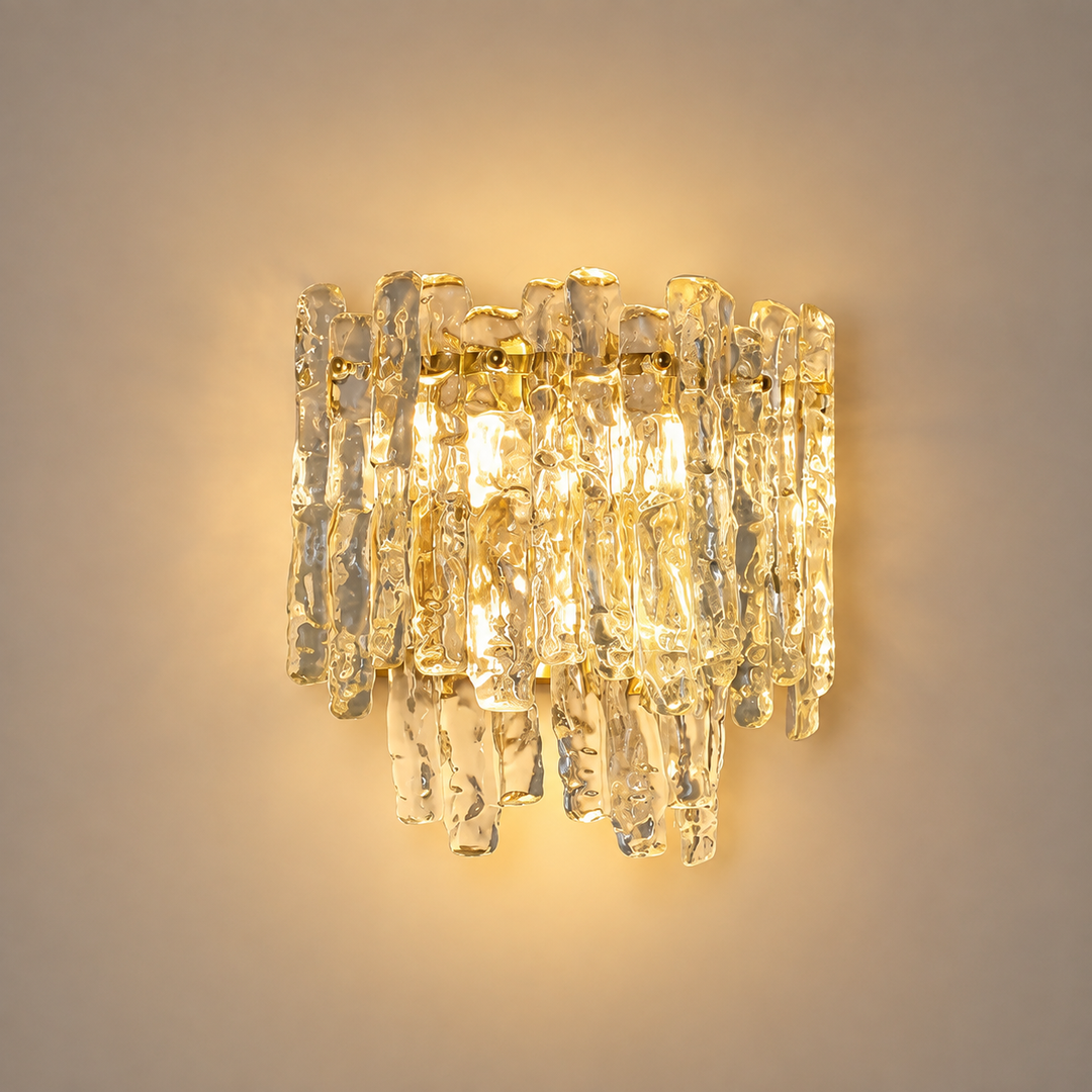 Wall sconce with hand-textured amber glass tiers cascading over a brass-tone frame, glowing warm against a plain beige wall.