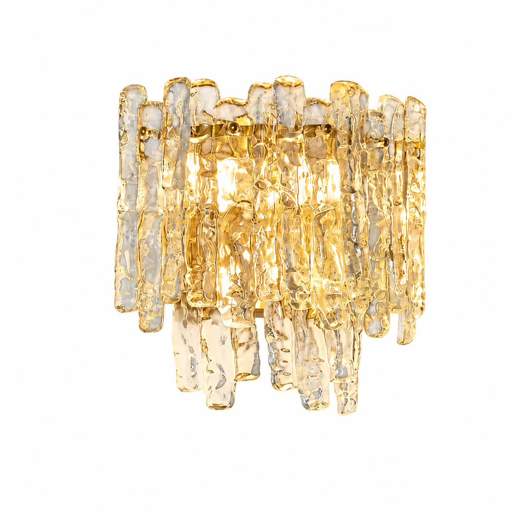 Illuminated wall sconce with textured clear glass rods, gold-toned fittings, and warm light against a white background.