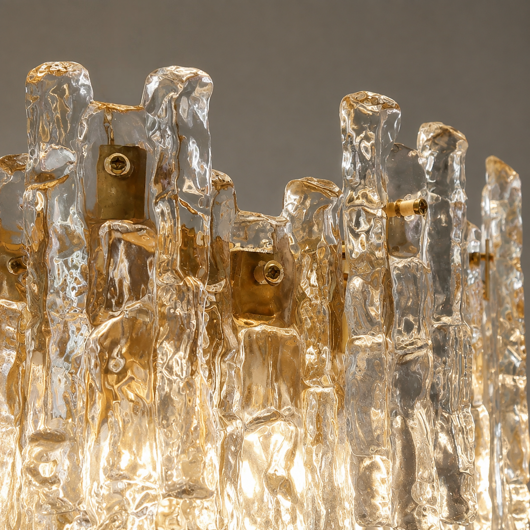 Close-up of the wall sconce's hand-textured amber glass tiers and brass-tone fittings glowing warmly against a grey background.