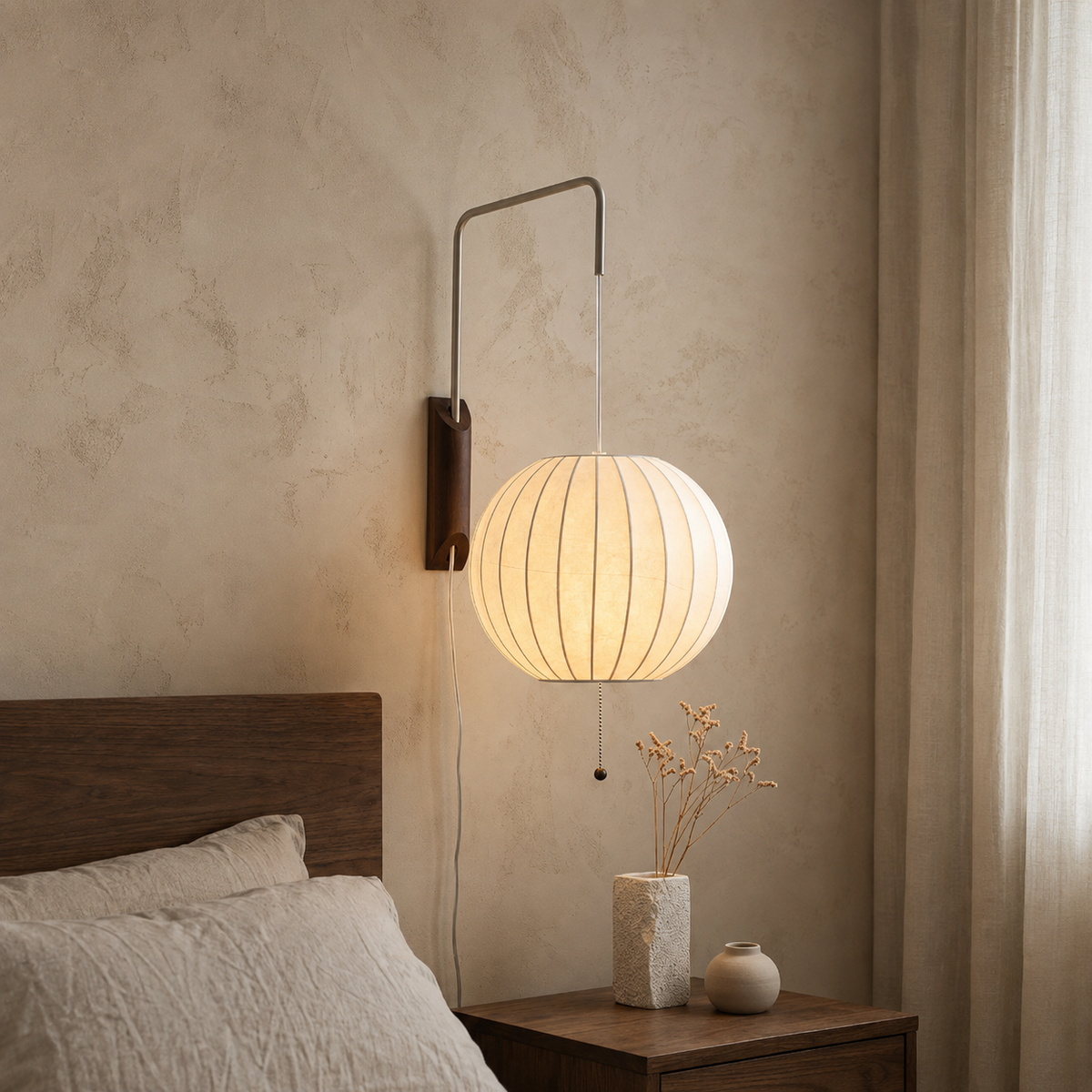 Wall sconce with a glowing round cream shade and walnut wood backplate above a bedside table beside sheer curtains.