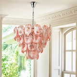 A modern chandelier with a cascading cluster of translucent blush pink glass discs on a polished silver metal frame, hanging in a bright, classic white hallway.