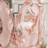 Close-up of a wall sconce showing textured pink glass panels and chrome supports against a blurred indoor background.