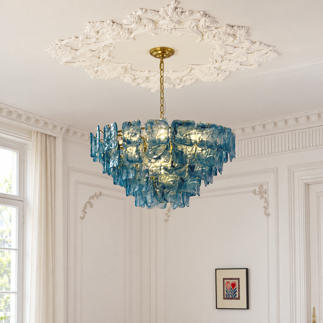 A blue glass chandelier with a gold ceiling mount hanging in an elegant white room with decorative wall molding and a white ornate ceiling medallion.
