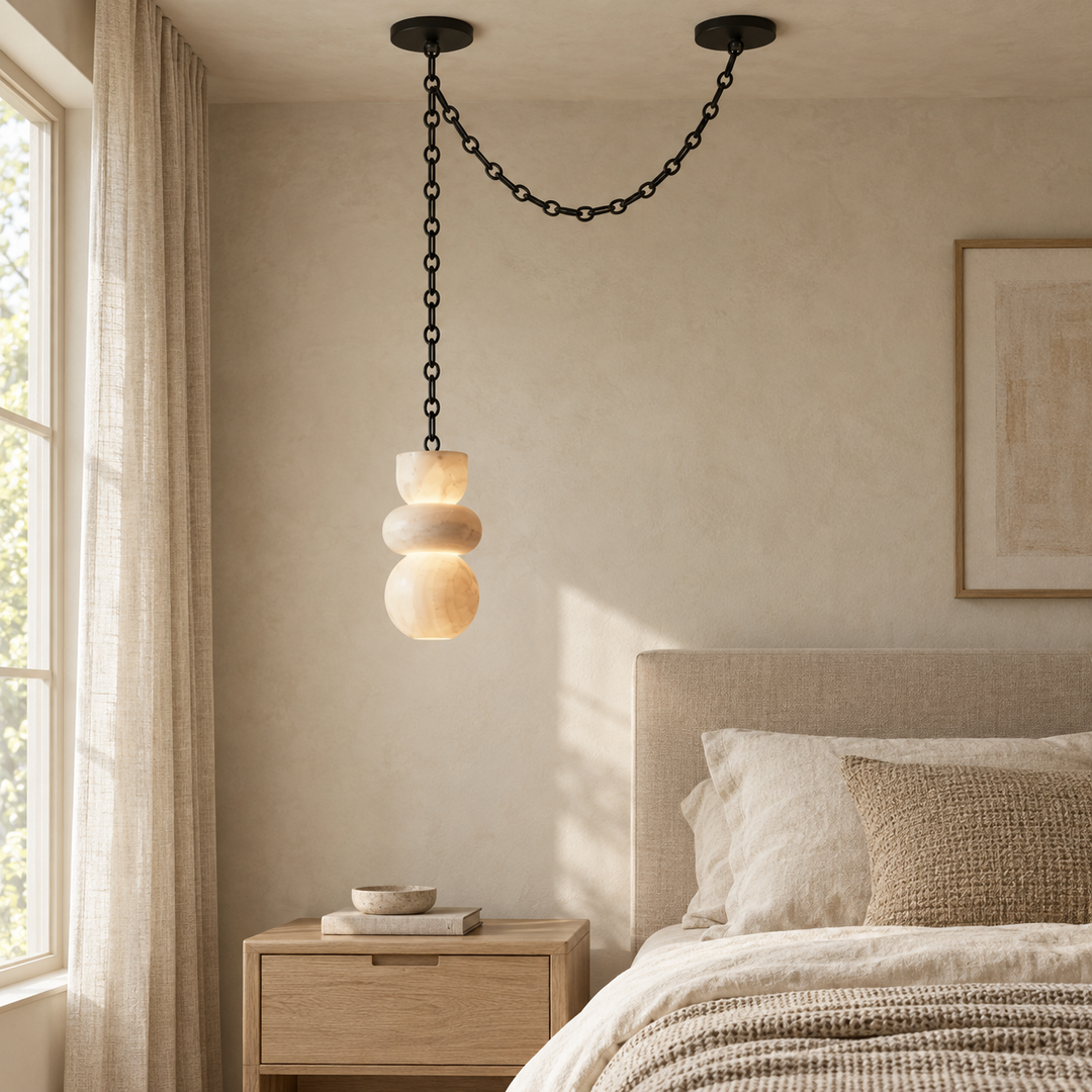 A cream marble chandelier hangs beside a bed, with its black chain draped between two ceiling mounts.