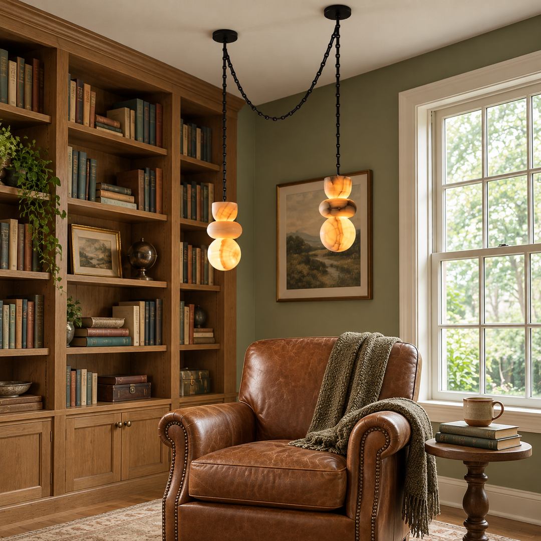 A two-light marble chandelier with black chains hangs above a brown leather armchair beside wooden bookshelves.