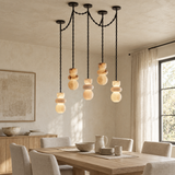A modern multi-light pendant chandelier with five stacked frosted glass shades on black chains, hanging over a dining table in a warm, neutral-toned room.