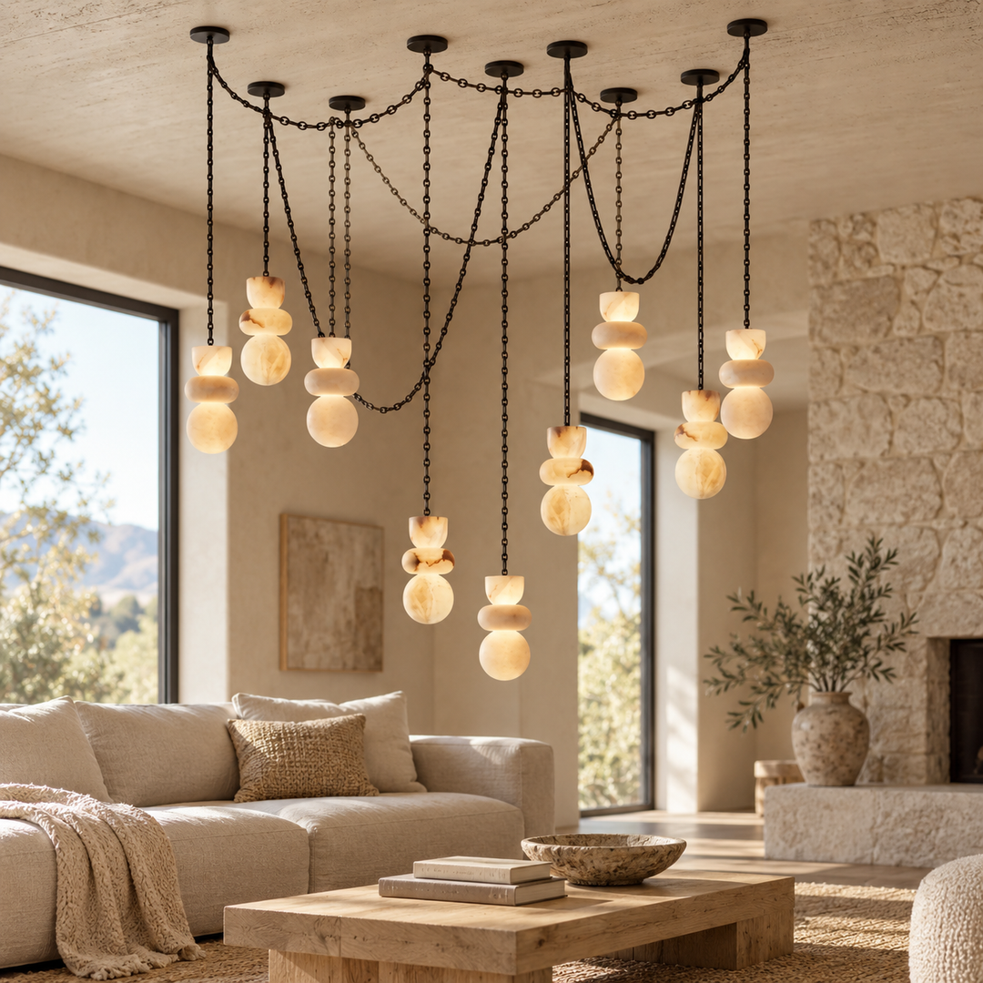 A modern multi-light pendant chandelier with black metal chains and multiple stacked frosted glass shades, hanging in a warm, contemporary living room with a beige sofa, stone fireplace, and large windows.