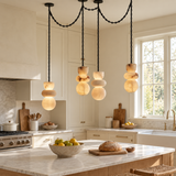 A modern kitchen with cream cabinetry and a marble island, featuring a black multi-light pendant chandelier with stacked organic-shaped glass shades glowing warm yellow.