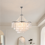 A multi-tiered crystal chandelier with a silver-toned metal frame and hanging glass beads, suspended from the ceiling in a bright, modern room.