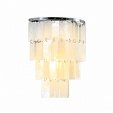 Illuminated wall sconce with tiered cream capiz shell panels and a silver-tone frame against a white background.