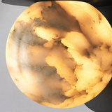 Close-up of the wall sconce’s glowing alabaster globe, showing cream and brown veining beneath a black metal cap.