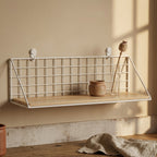 White wire grid wall shelf styled with a small stoneware pot and a single dried stem