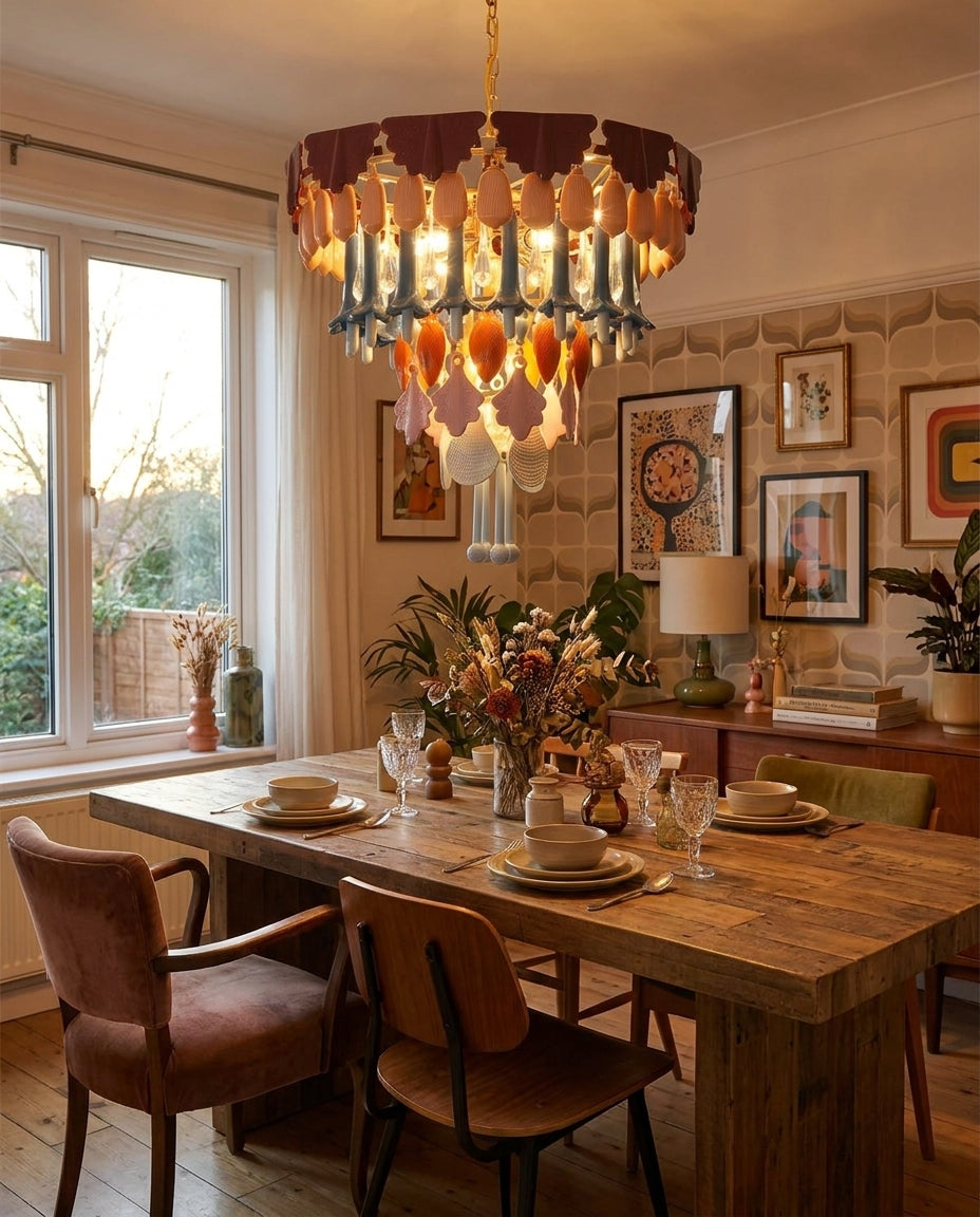 A bohemian-style chandelier with layered amber and orange glass discs, blue glass accents, and hanging crystal prisms, suspended over a rustic wooden dining table in a warmly lit dining room.