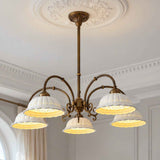 An ornate five-light chandelier with a bronze-finished metal frame and white lace-detailed bell shades, illuminated in a classic European-style room with white walls and molding.